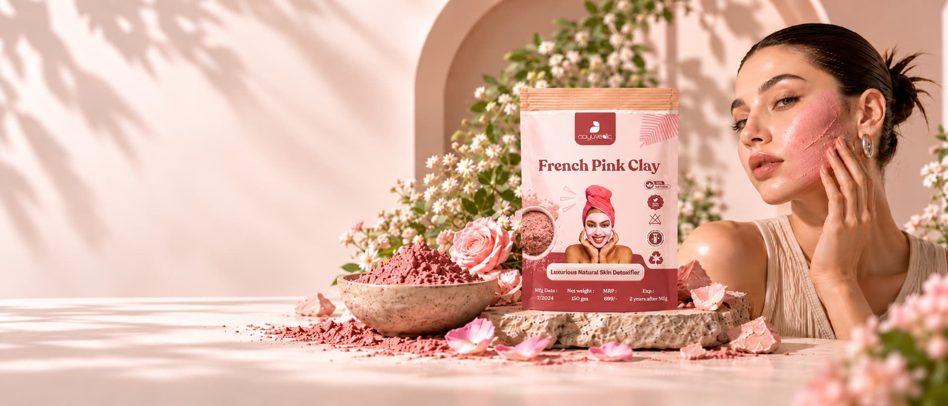 French Pink Clay pouch beside a bowl of pink clay and roses, with a woman wearing the clay mask